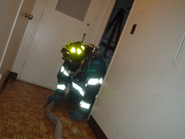 With blackened face masks, members train on following a hose line in a simulated smoke condition